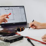 Close-up of hands sketching design plans with tile samples and a laptop, ideal for interior design contexts.