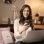 A woman enjoying leisure time using her smartphone and laptop in a cozy living room.